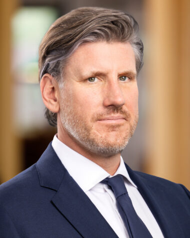 Close-up portrait of a middle-aged man in a navy suit and white shirt, looking off to the side.